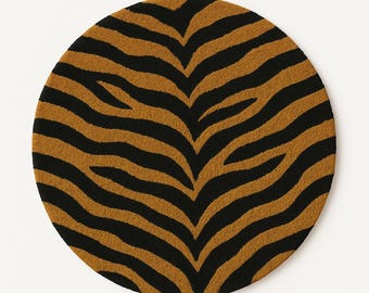 May include: Round rug with a tiger stripe pattern. The rug features alternating black and tan stripes, creating a bold, animal print design. The rug is circular and appears to be made of a soft, textured material.