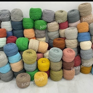 May include: A large collection of yarn balls in various colors including green, blue, yellow, grey, brown, and beige. The yarn balls are stacked in a dense arrangement, and the text AnayatRugs is visible in several locations across the image.