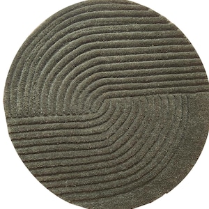 Op de afbeelding: Een ronde, donkergrijze vloerkleed met een getextureerd oppervlak. Het vloerkleed heeft een geometrisch ontwerp van gebogen lijnen, waardoor een patroon ontstaat. Het ontwerp van het vloerkleed is een halve cirkel met een reeks parallelle lijnen.