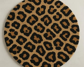 May include: A round rug with a leopard print design. The rug features a tan background with black and brown spots, creating a classic animal print pattern. The rug is circular in shape.