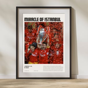 May include: A black and white framed poster with the text "Miracle of Istanbul" in bold white letters. The poster features a photo of a group of soccer players celebrating with a trophy, surrounded by red confetti. The text "Liverpool FC vs. AC Milan" and the date "25 May 2005" are also included on the poster.