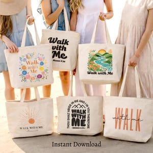 May include: Six off-white canvas tote bags featuring various designs with the text Walk with Me and Moses 6:34. The bags display colourful floral wreaths, a landscape with a river and sun, a sunburst graphic, and bold typography in black and orange.