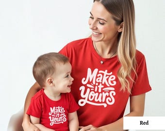 May include: A red t-shirt with the text "Make it Yours" in white. A matching red t-shirt with the same text is worn by a child. The shirts are on a white background.