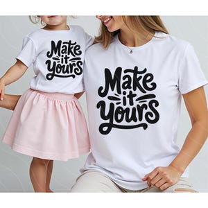 Könnte beinhalten: Zwei weiße T-Shirts mit schwarzem Text, der "Make it yours" lautet. Die Shirts werden von einer Frau und einem Kind getragen.