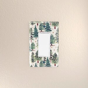 May include: A white light switch cover with a green and white pattern of stylized pine trees and gold stars.