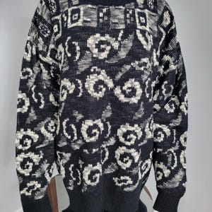 May include: Black and white patterned sweater with a crew neck and long sleeves. The sweater features a repeating floral and geometric design. The cuffs and hem are solid black. The sweater is displayed on a mannequin.