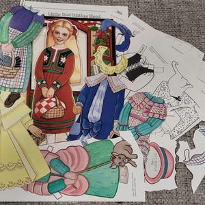 K&ouml;nnte beinhalten: Eine Sammlung von Vintage-Papierpuppen und -Outfits mit Illustrationen aus "Rotk&auml;ppchen". Das Set enth&auml;lt ein M&auml;dchen in einem roten Kleid, eine Frau in einem gr&uuml;nen und lila Kleid und verschiedene Kleidungsst&uuml;cke in Gelb, Blau und Rosa. Einige Teile sind ausgeschnitten.