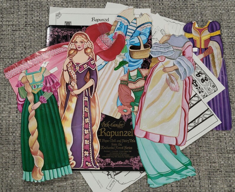 K&ouml;nnte beinhalten: Eine Sammlung von Vintage-Papierpuppen und Outfits mit dem Thema Rapunzel. Die Puppen sind in farbenfrohen Kleidern und Gew&auml;ndern mit langen, flie&szlig;enden Haaren dargestellt. Das Set enth&auml;lt eine Puppe, Outfits und ein Heft.