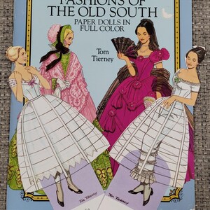 K&ouml;nnte beinhalten: Ein Vintage-Papierpuppenbuch mit dem Titel "Fashions of the Old South" mit Illustrationen von Frauen in historischen Kleidern. Das Cover zeigt vier Frauen in farbenfrohen Kleidern, mit zwei Papierpuppen mit der Aufschrift "Amelia" und "Tracy".