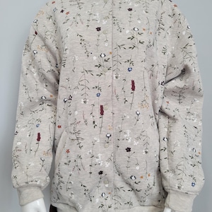 May include: A light gray bomber jacket with a floral pattern. The jacket features a button-up front, ribbed cuffs, and a ribbed hem. The floral design includes white, red, blue, and brown flowers and green leaves.