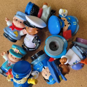 May include: A collection of Fisher-Price Little People plastic figures featuring various characters in uniform, including sailors, pilots, and train conductors. The figures are painted in blue, white, red, and black, with some showing the Little People logo.