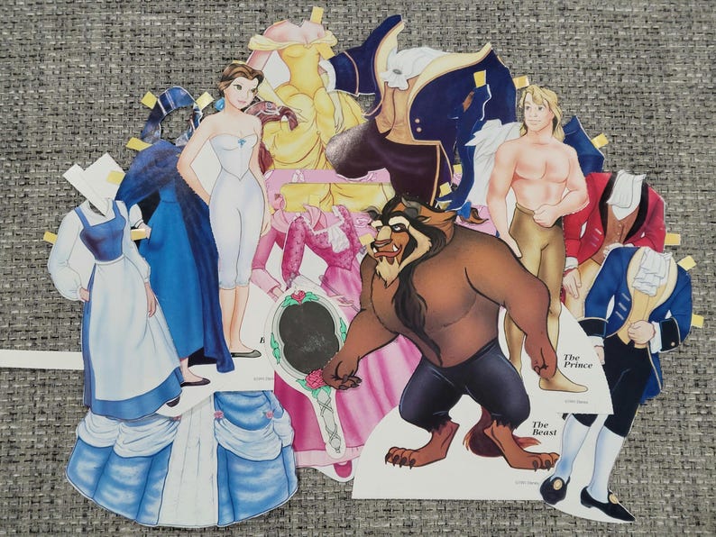 K&ouml;nnte beinhalten: Papierpuppen mit Charakteren aus Disneys Die Sch&ouml;ne und das Biest. Enth&auml;lt Belle, das Biest, Gaston und andere Charaktere. Die Puppen haben Outfits und Accessoires in verschiedenen Farben, darunter Blau, Gelb und Rosa.
