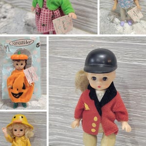 May include: A collection of five Madame Alexander dolls featuring various outfits including a ladybug costume, a floral top with pants, a pumpkin suit, a yellow raincoat with a duck hat, and a red equestrian jacket with a black riding helmet.