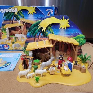 May include: A Playmobil nativity scene set with figures, animals, and buildings. The set includes a stable, figures of Mary, Joseph, and baby Jesus, and various animals. The box shows a similar scene with palm trees and a star.