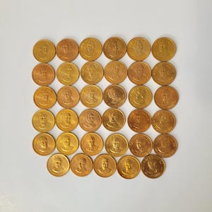May include: A collection of gold-coloured coins, each featuring a portrait of a person on one side. The coins are arranged in a grid pattern against a white background. The coins appear to be made of metal.