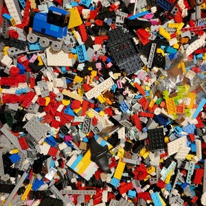 Puede incluir: Una gran colección de bloques de construcción de plástico surtidos en varias formas, tamaños y colores, incluyendo rojo, azul, amarillo, negro, blanco y gris. El montón incluye una pequeña locomotora azul y una pieza de plástico negra con forma de murciélago.