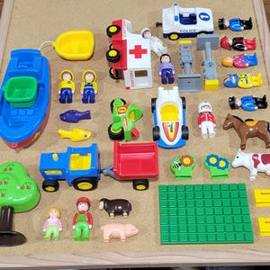May include: A collection of colorful toy vehicles, figures, and accessories, including a blue boat, ambulance, police car, and a green motorcycle. Other items include a tree, farm animals, and a green play mat.
