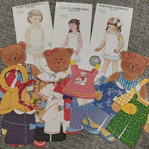 K&ouml;nnte beinhalten: Eine Sammlung von Vintage-Papierpuppen und b&auml;renf&ouml;rmigen Papierpuppen mit Outfits. Die Papierpuppen sind von M&auml;dchen namens Suzette, Marian und Dorothy. Die Outfits umfassen Kleider, Overalls und M&auml;ntel in verschiedenen Mustern und Farben.