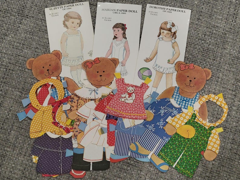 K&ouml;nnte beinhalten: Eine Sammlung von Vintage-Papierpuppen und b&auml;renf&ouml;rmigen Papierpuppen mit Outfits. Die Papierpuppen sind von M&auml;dchen namens Suzette, Marian und Dorothy. Die Outfits umfassen Kleider, Overalls und M&auml;ntel in verschiedenen Mustern und Farben.