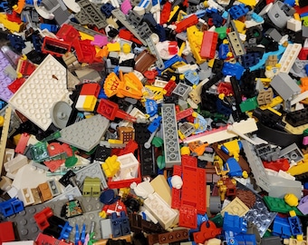 Può includere: Una grande collezione disorganizzata di mattoncini da costruzione e componenti in plastica assortiti di varie forme, dimensioni e colori, inclusi pezzi rossi, blu, gialli, verdi, grigi, bianchi e neri sparsi insieme in un mucchio.