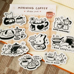 Puede incluir: Un paquete de pegatinas con las palabras "MORNING COFFEE" y "sticker pack" impresas en la parte superior. El paquete contiene nueve pegatinas con ilustraciones en blanco y negro de conejos, tazas de café y equipo para hacer café. Algunas pegatinas tienen texto como "¡BUEN PROVECHO!"