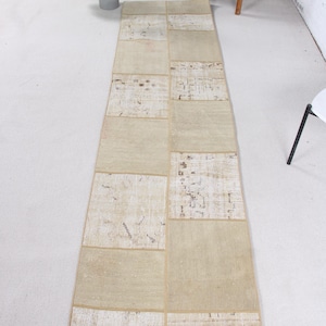 May include: A rectangular, beige patchwork rug with a variety of textured squares. The rug is long and narrow, suitable for a hallway or entryway. The squares have different patterns and shades of beige.