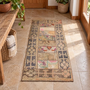 May include: A rectangular runner rug featuring a patchwork design of various faded textile segments in muted tones of brown, gray, and beige, accented with small floral motifs in pink and orange, framed by a dark geometric border pattern.