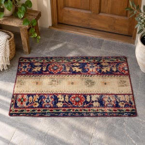 May include: A rectangular area rug featuring a central beige band flanked by two wide borders in deep blue, red, and green. The borders display intricate floral and geometric patterns, while the beige center contains subtle, faded motifs.