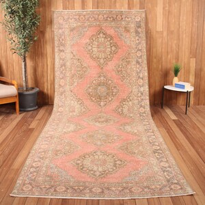 Peut inclure: Un long tapis rectangulaire présentant un fond rose saumon avec une série répétée de grands médaillons floraux complexes dans des tons beige, taupe et bleu sourd, encadré par une bordure détaillée aux motifs géométriques.