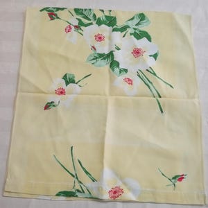 May include: A yellow pillowcase featuring a floral pattern of white roses with red centers and green leaves. The roses are clustered in several areas across the pillowcase. The background is a solid, pale yellow color.