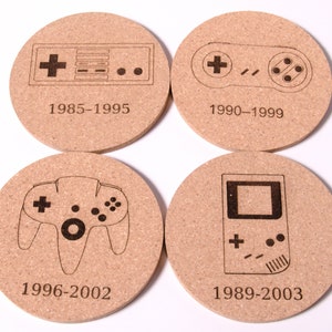 May include: Four round cork coasters with black and white illustrations of video game controllers and handheld consoles. Each coaster has a year range printed below the image. The coasters are: 1985-1995, 1990-1999, 1996-2002, and 1989-2003.