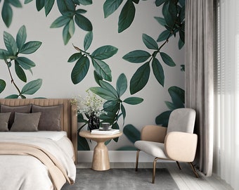 May include: A bedroom interior with a bed, a chair, and a side table. The wall behind the bed is covered in a wallpaper with a large-scale leaf pattern. The chair is upholstered in a light gray fabric and has a beige cushion. The side table is made of wood and has a round top. The room is decorated in a modern style.