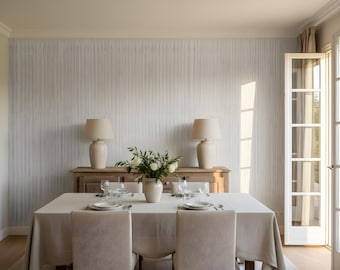 May include: A dining room scene featuring a table set for a meal. The table is covered with a white tablecloth and set with plates, glasses, and silverware. Two cream-colored lamps sit on a wooden sideboard. A vase of white flowers is in the center.