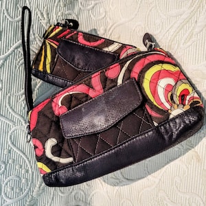 May include: Two small, quilted clutch bags with a colorful, retro-style pattern in red, yellow, and white on a dark brown background. Each bag has a dark blue leather trim and a small pocket. One has a wrist strap.