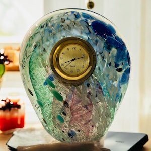 May include: A glass clock with a blue, green, and white abstract design. The clock face is gold with black hands and the word "Quartz" printed on it.