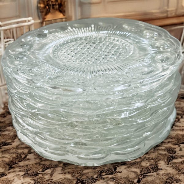 May include: A stack of clear glass plates with a decorative, raised design. The plates are stacked on top of each other, creating a layered effect.
