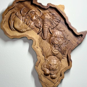 May include: A wooden carving in the shape of Africa, depicting an elephant, lion, rhino, and tiger in relief. The artwork is crafted from light brown wood, showcasing intricate details.