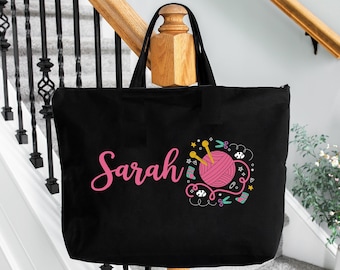 May include: Black tote bag with a pink yarn ball and knitting needles design. The bag has the name "Sarah" printed in pink.