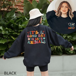 May include: Black sweatshirt with a colorful graphic that says "It's a good day to save animals". The graphic features paw prints, hearts, and bones. The sweatshirt is shown on a model wearing black shorts.