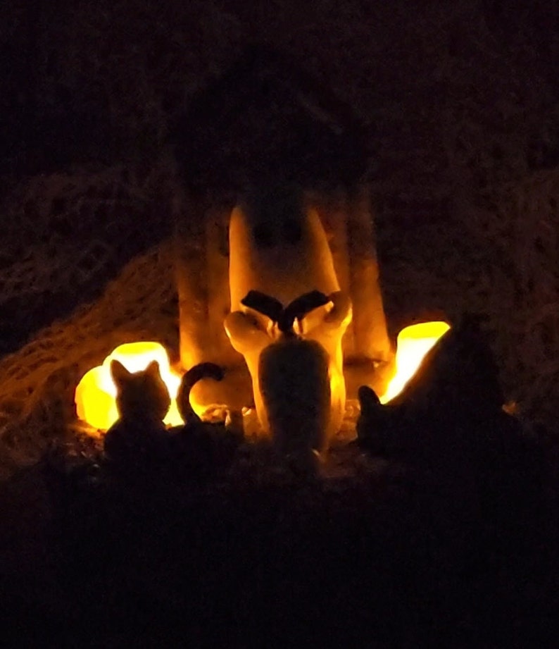 Dark photo to show flickering candles. Ghost sitting beside gravestone reading a book with 2 black cats playing in the fall leaves. Halloween decor that will glow in the dark and has flickering candles.