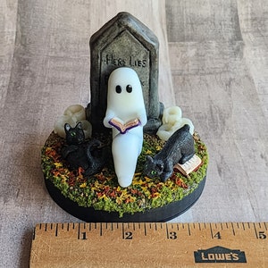 Sculpt is on a round 4 inch base. Ghost sitting beside gravestone reading a book with 2 black cats playing in the fall leaves. Halloween decor that will glow in the dark and has flickering candles.