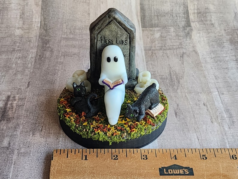 Sculpt is on a round 4 inch base. Ghost sitting beside gravestone reading a book with 2 black cats playing in the fall leaves. Halloween decor that will glow in the dark and has flickering candles.
