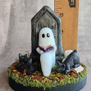 Sculpt is approximately 3.75 inches tall. Ghost sitting beside gravestone reading a book with 2 black cats playing in the fall leaves. Halloween decor that will glow in the dark and has flickering candles.