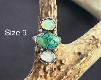 May include: A silver ring with three stones. The center stone is a green turquoise, and the two smaller stones are white opals. The ring is size 9.