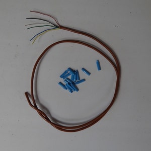 May include: A brown wire with six different colored wires coming out of it. The wire is coiled into a circle. There are a pile of blue wire connectors on a white surface.