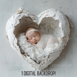 May include: A newborn baby sleeping in a white heart-shaped prop with a white fuzzy blanket. The heart is cracked and has a rough texture. The baby is wearing a white swaddle and a white headband.