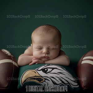 Può includere: Un neonato dorme su un cuscino verde e bianco con un disegno di un'aquila. Il cuscino è circondato da due palloni da calcio marroni. Lo sfondo è verde solido.