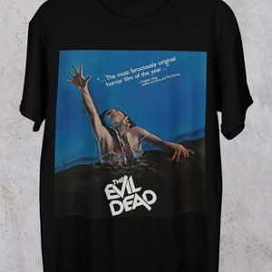 May include: Black t-shirt with a graphic print of a movie poster for "The Evil Dead". The poster features a woman reaching out of a muddy grave with the text "The most ferociously original horror film of the year..." and "Stephen King, author of Carrie and The Shining".