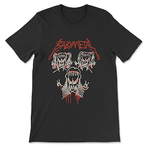 Pode incluir: Camiseta preta com um gr&aacute;fico branco de tr&ecirc;s figuras de desenhos animados com acentos vermelhos. O texto "BABYMETAL" est&aacute; escrito em vermelho acima das figuras.