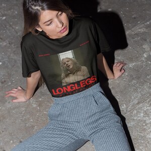 Puede incluir: Una camiseta negra con un estampado gr&aacute;fico de una mujer con el texto "LONGLESS" en rojo. La mujer lleva una camisa marr&oacute;n claro y tiene el pelo rubio. El texto "KILLA BEAST" est&aacute; en blanco en la parte superior del gr&aacute;fico. El texto "WICKED GAME" est&aacute; en blanco en la parte inferior del gr&aacute;fico.